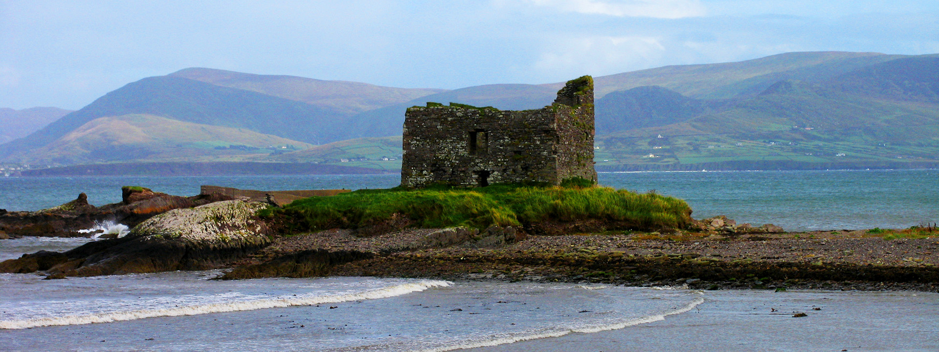 Eine Burgruine steht auf einer Landzunge an der Küste Irlands.
