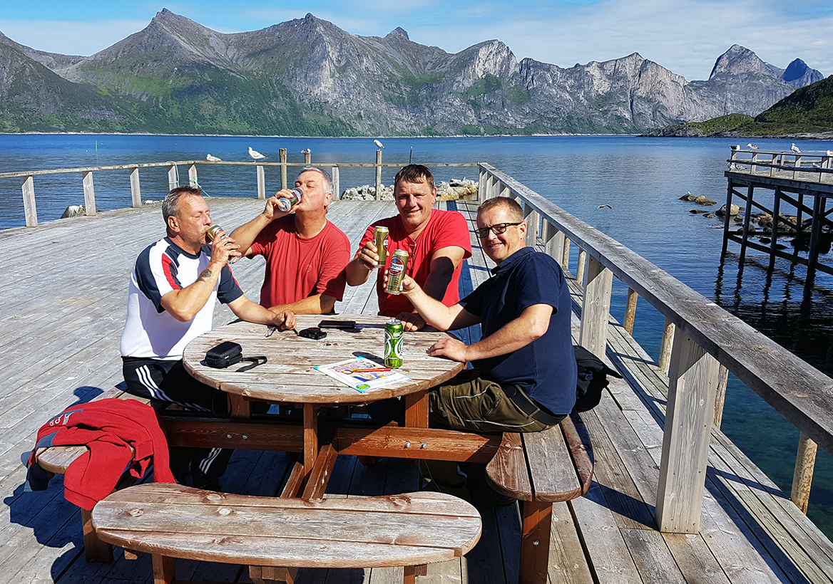 Mehrere Angler trinken an einem Hafen in der Mefjord Brygge gemeinsam ein Bier. 