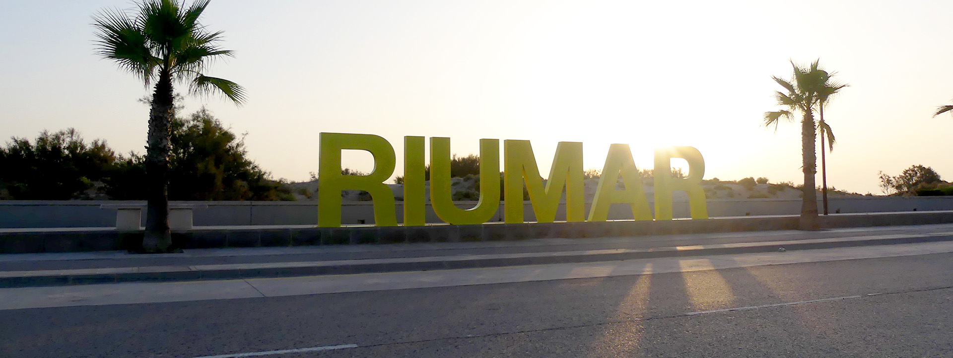 Ein Schriftzug mit dem Namen der Stadt Riumar steht zwischen Palmen.